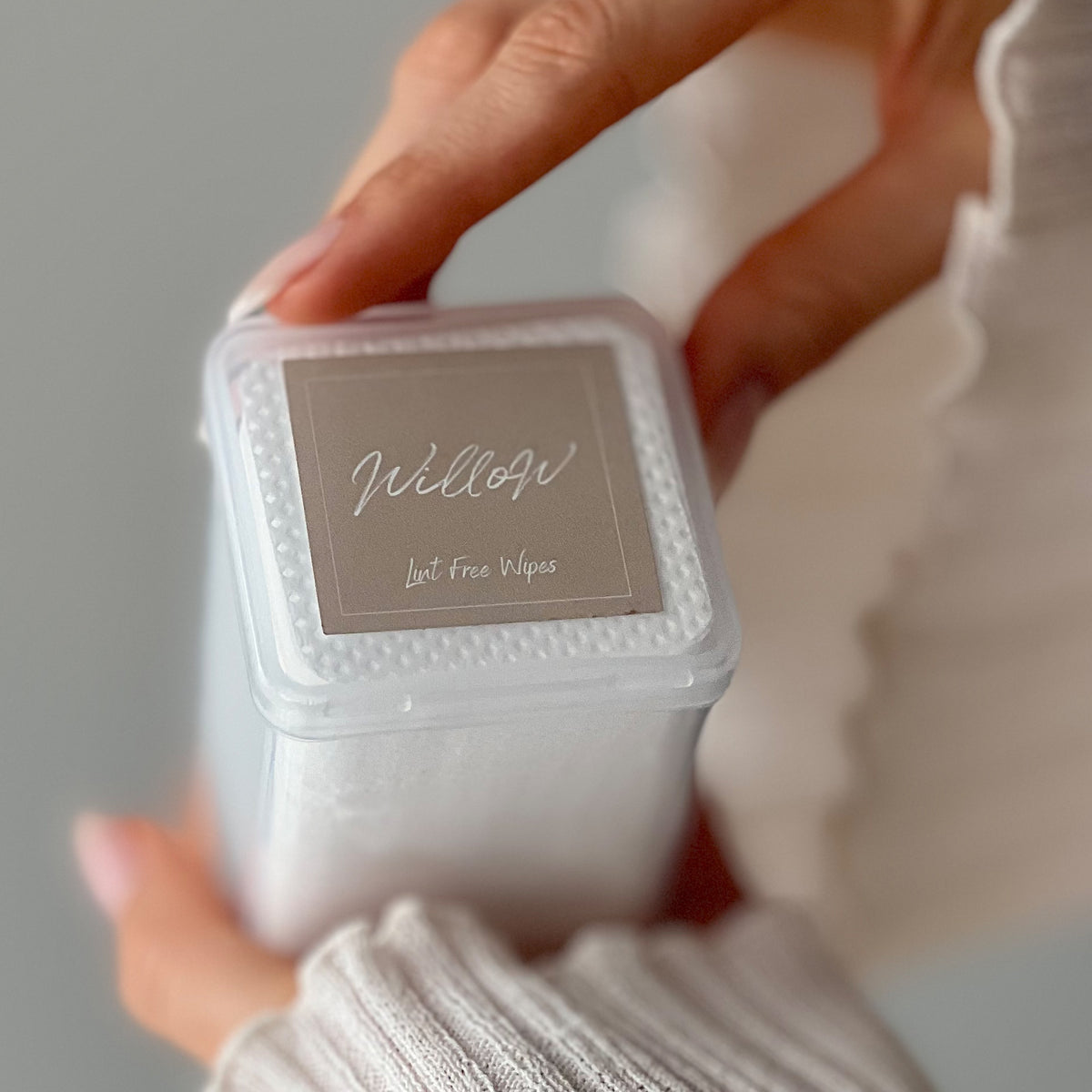 a hand holding a box of Willow lint free wipes with a flip top lid