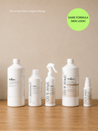 Five white Willow brand toiletry bottles and sprayers arranged on a wooden surface against a beige wall, with a green circular badge reading 'SAME FORMULA NEW LOOK!' in the top right.